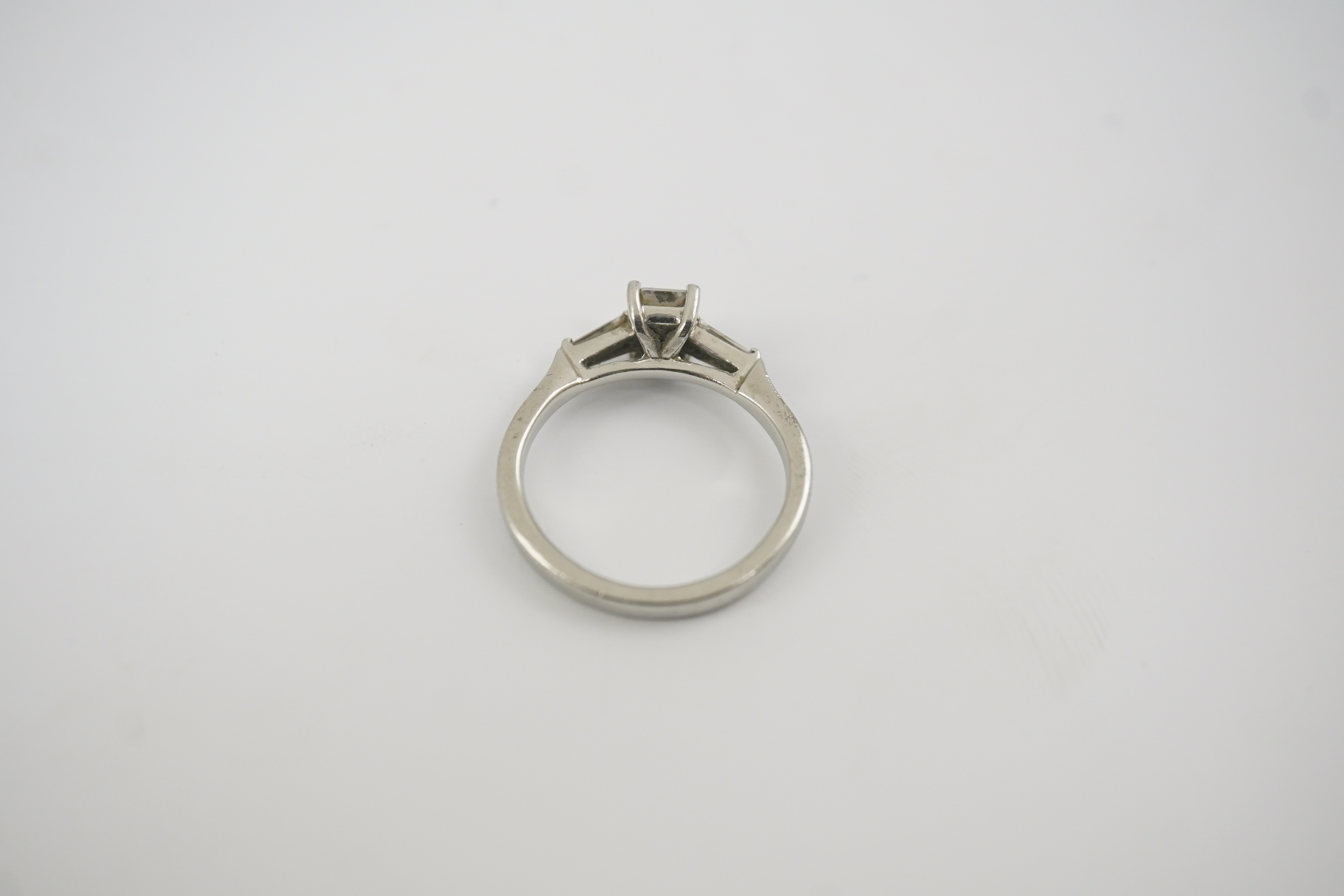 A modern platinum and single stone emerald cut diamond set ring, with two stone tapered baguette cut diamond set shoulders